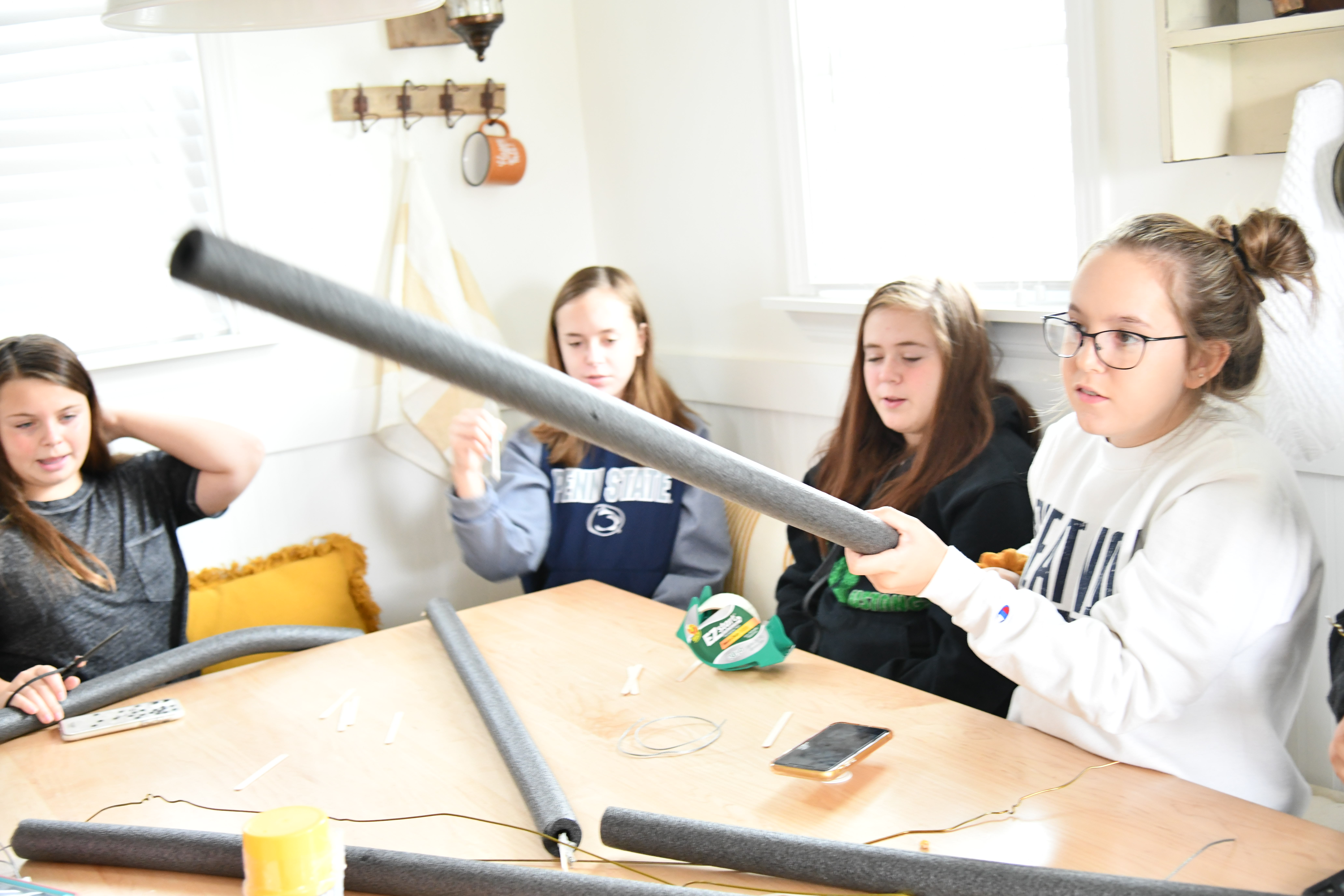 girls sitting at the table pushing wire through plumbers pipe for DIY