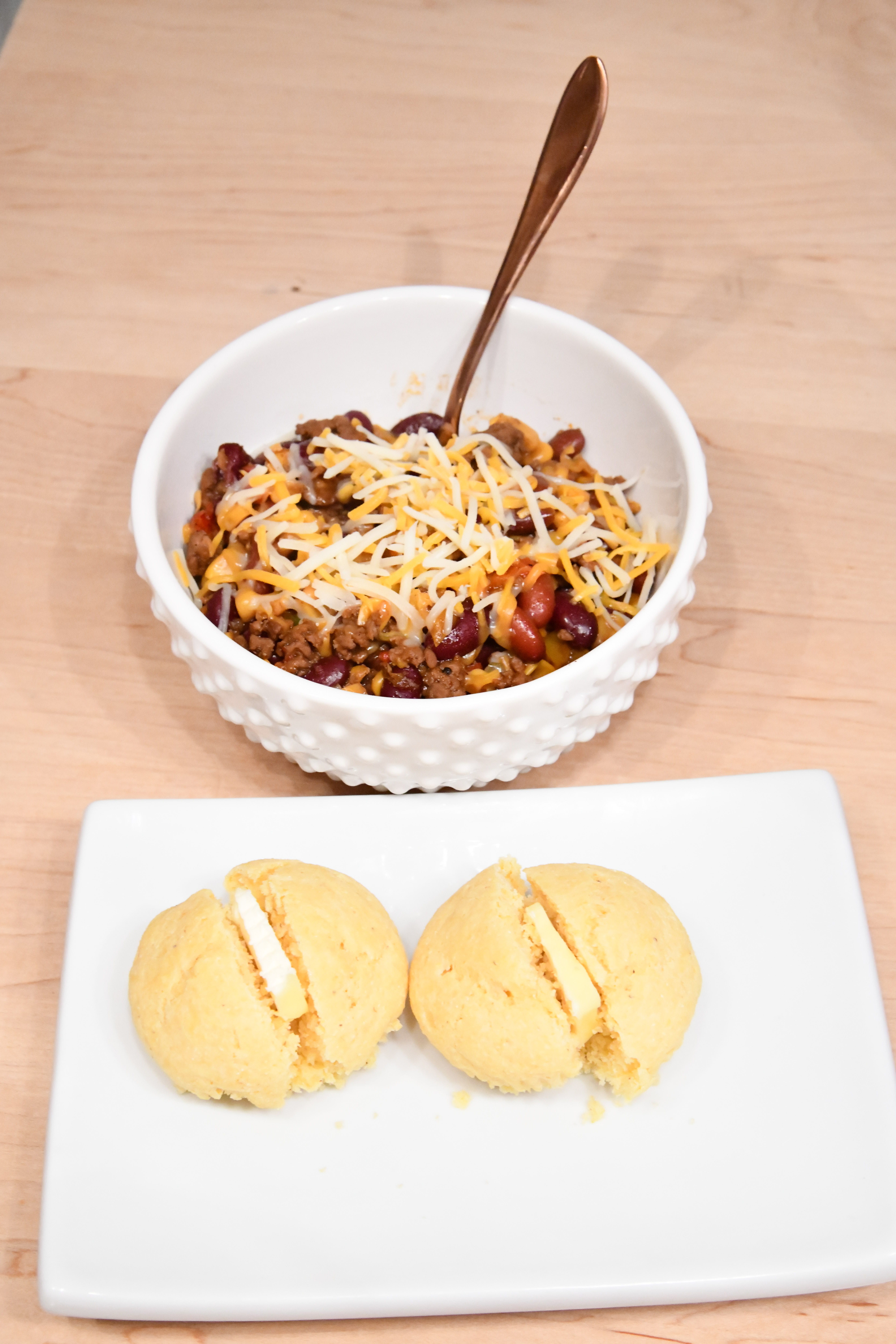Chili with cheese in bowl corn bread on plate with butter