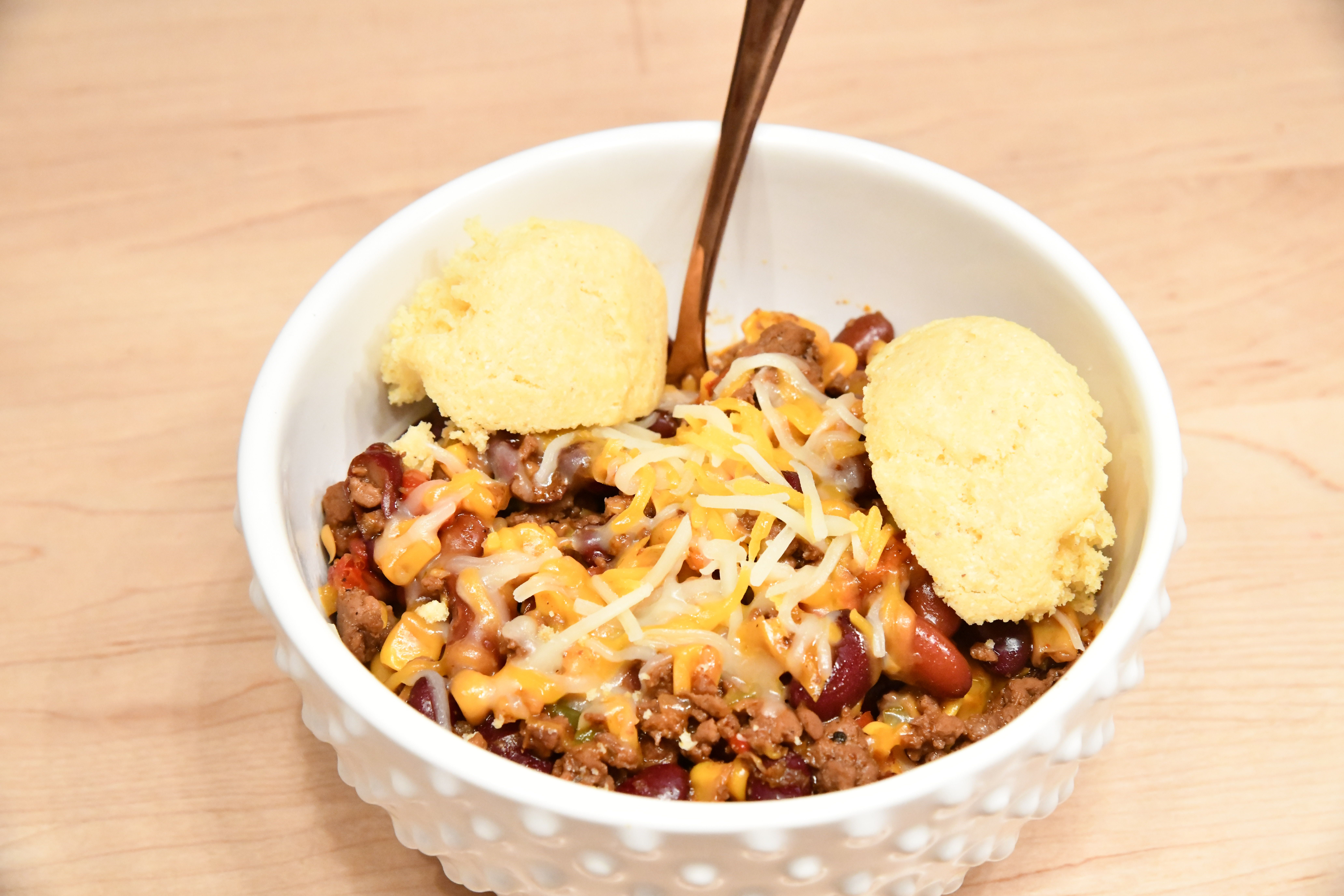 Chili with cheese and cornbread in a bowl on the counter