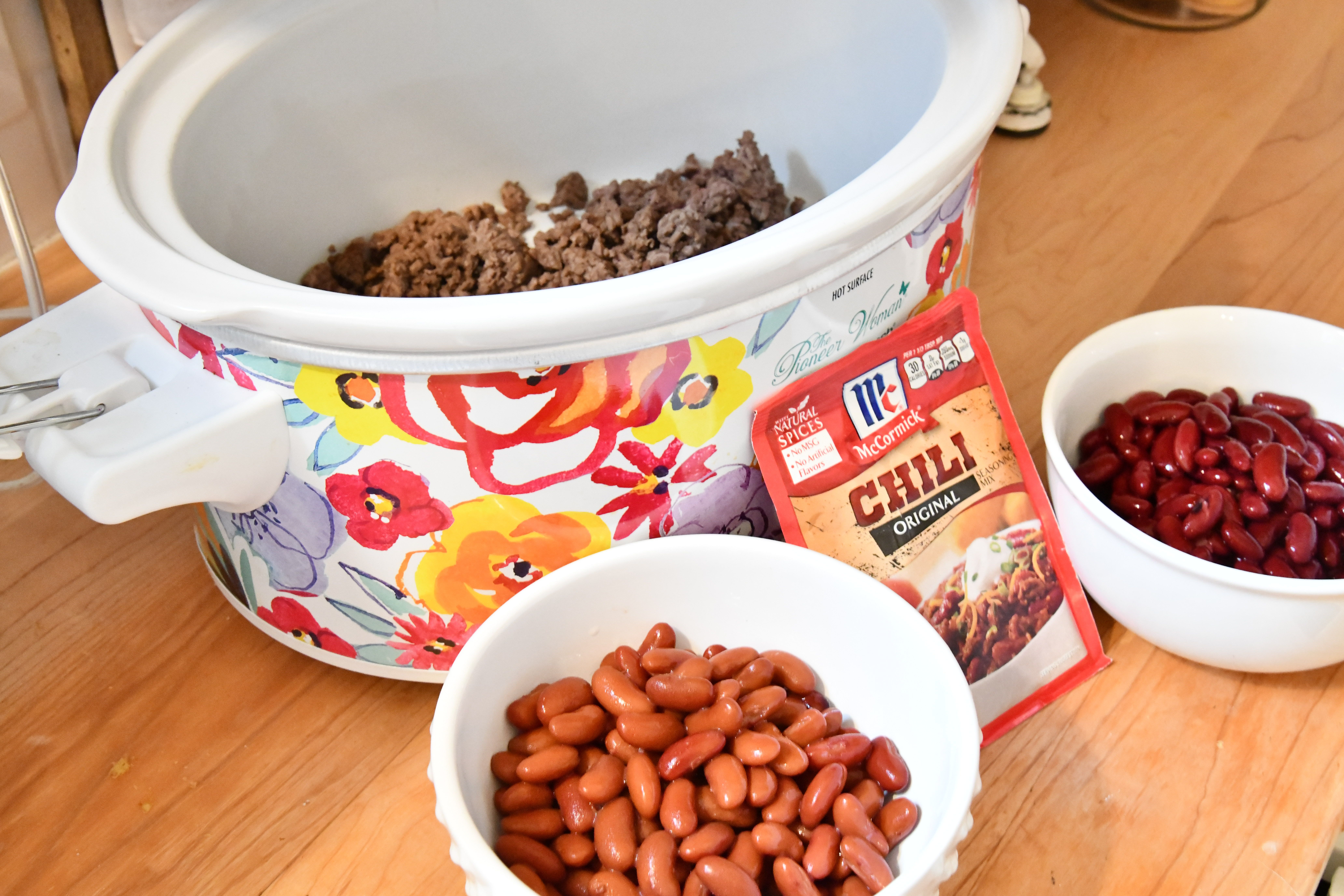 Crockpot with meat inside and bowls of kidney beans and hili mix on kitchen counter