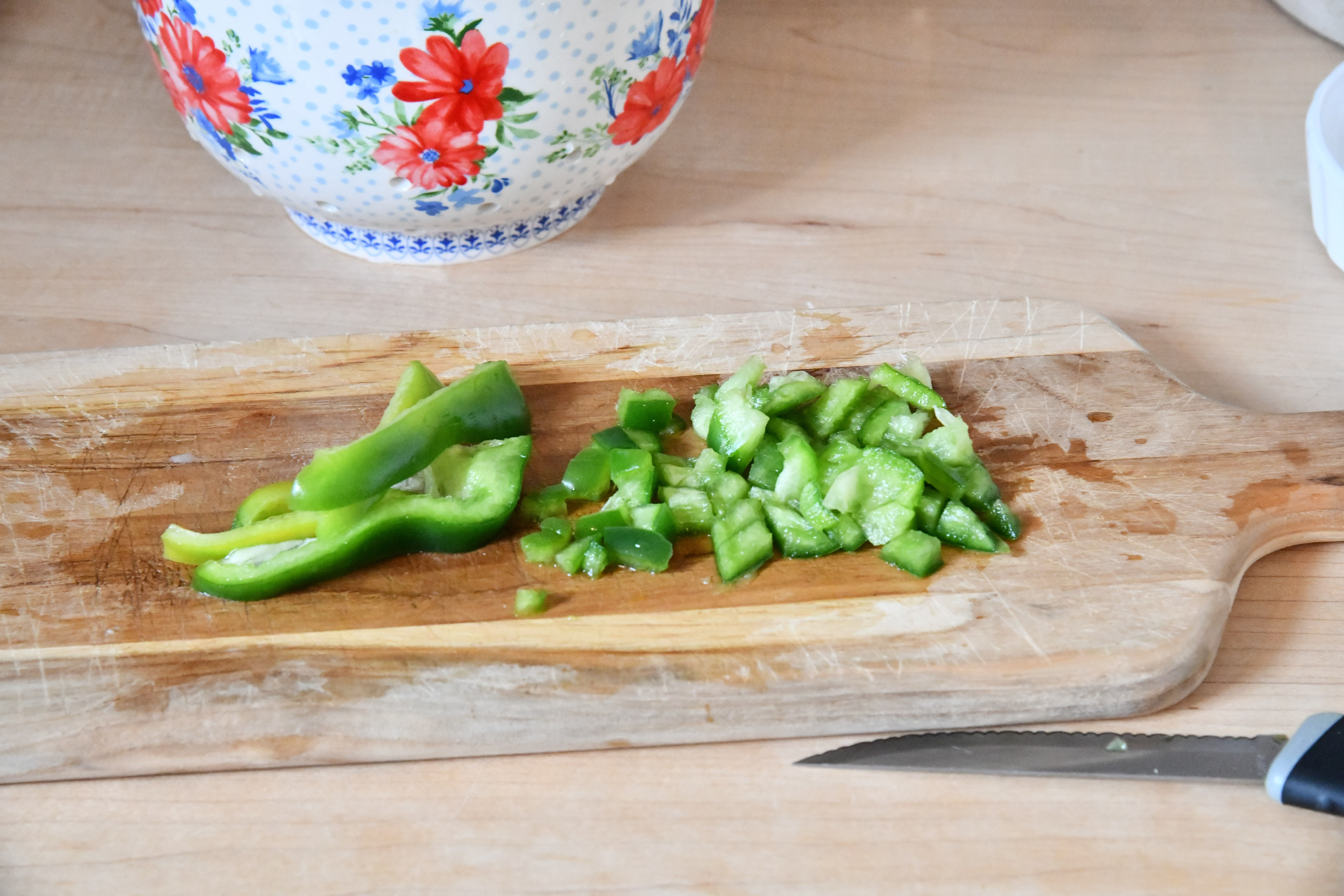 Sliced and diced green pepper on cutting board sitting on counter with strainer