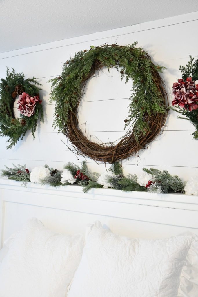One large wreath two smaller wreathes Christmas on shiplap wall and white bed farmhouse Christmas garland