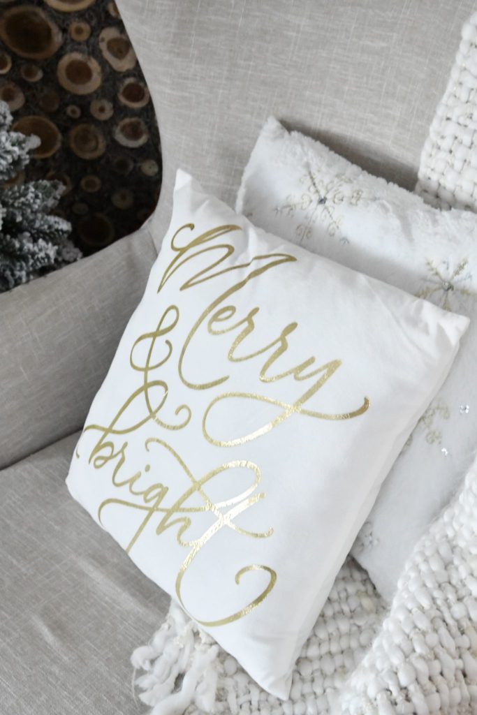 Merry & Bright White Christmas Pillow with gold writing sitting on chair