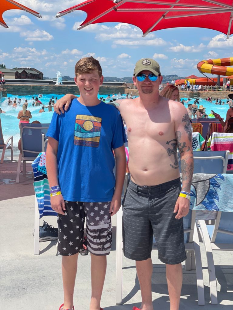 teenage boys and father in swim suits with water park wave pool and slide in the background