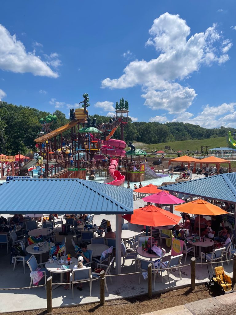 large view of water park with colorful slides and umbrellas people eating under outside covered food court