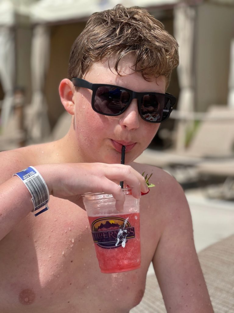teen boy with sunglasses by pool drinking strawberry milkshake