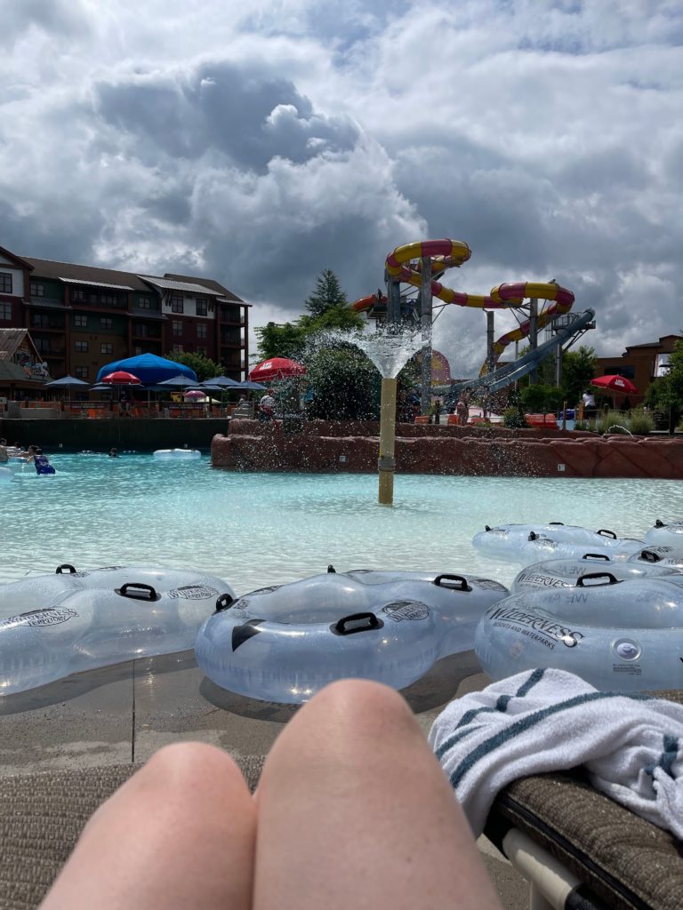 wilderness smokies outdoor water park lazy river ladies knees sitting on chair looking at water and tubes floating with hotel and waterslides in background
