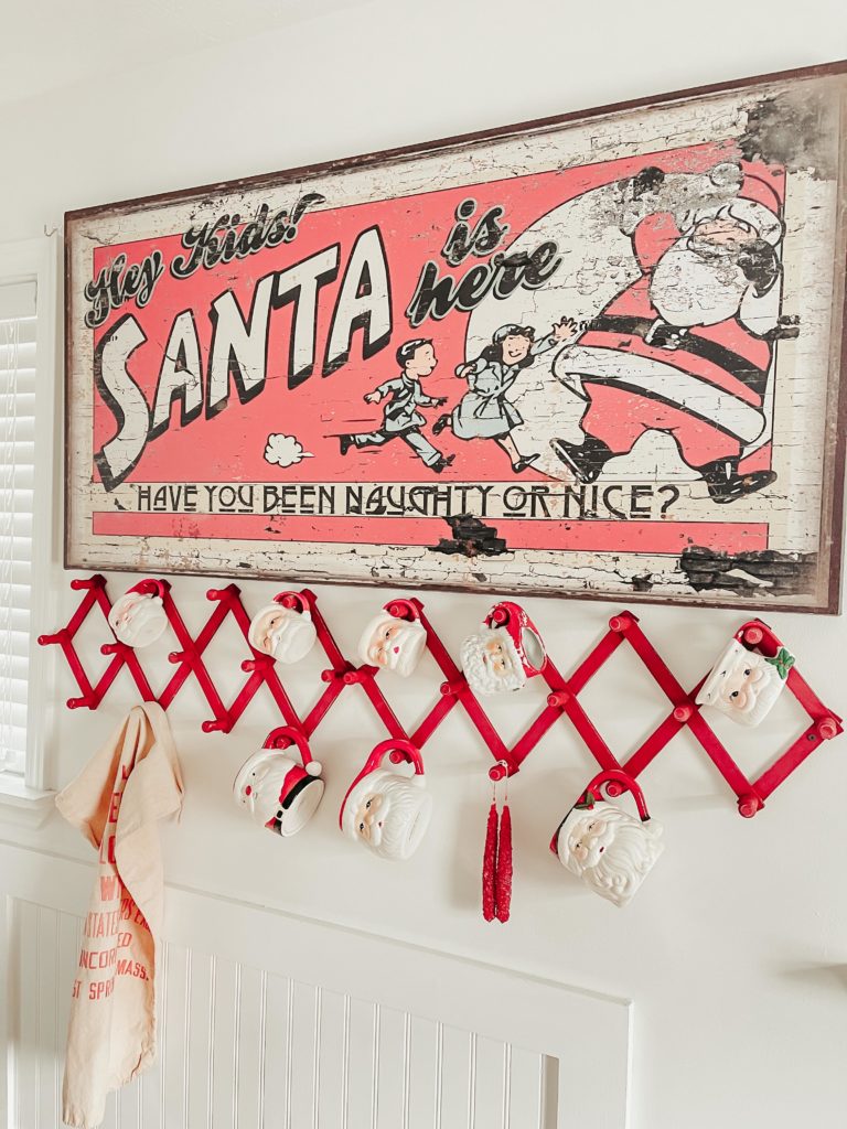 Santa is coming to town red and black sign on wall with Santa mugs hanging on rack