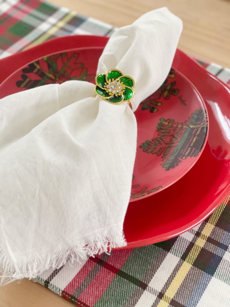 green and gold flower napkin ring on white napkin with red Christmas plate