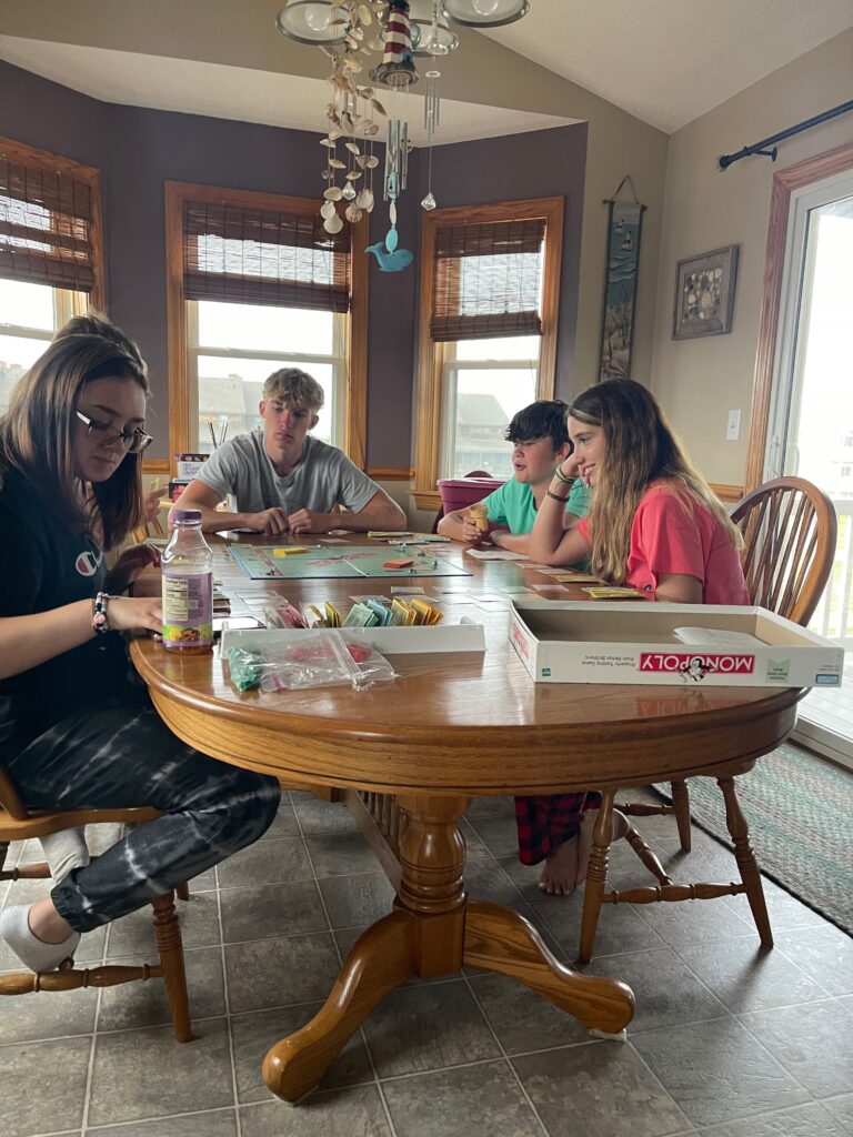 family sitting around a table playing Monopoly at beach rainy day