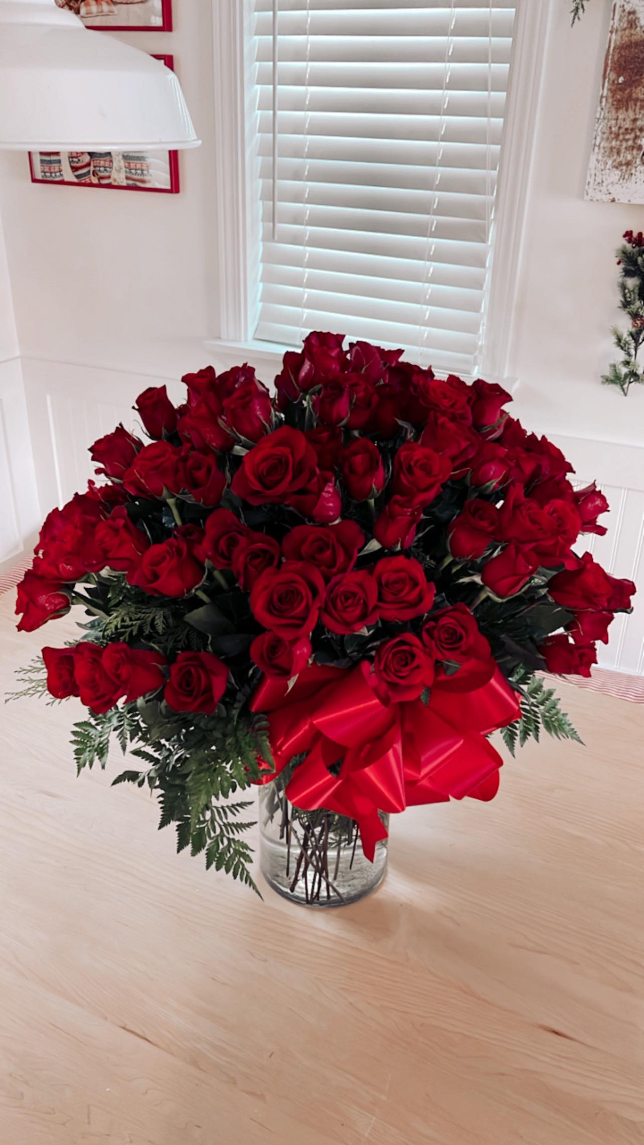 100 red stem long roses in clear vase on a table