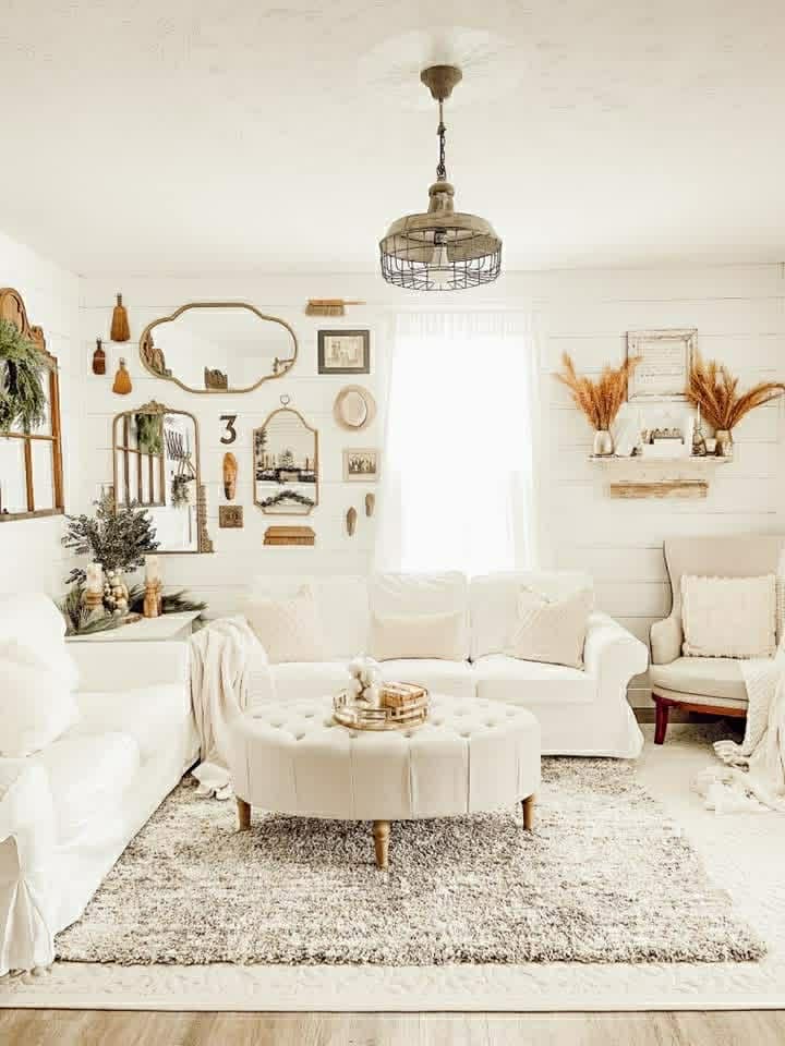 Farmhouse living room with white walls, warm wood furniture, and a vintage mirror
Neutral farmhouse living room featuring white textiles, wood accents, and antique decor
Cozy farmhouse living space styled with white, natural wood, and vintage charm